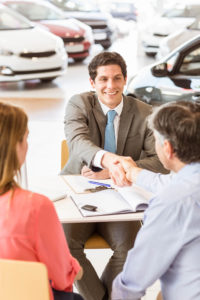 Couple at car dealer's desk shaking hands like they have a deal