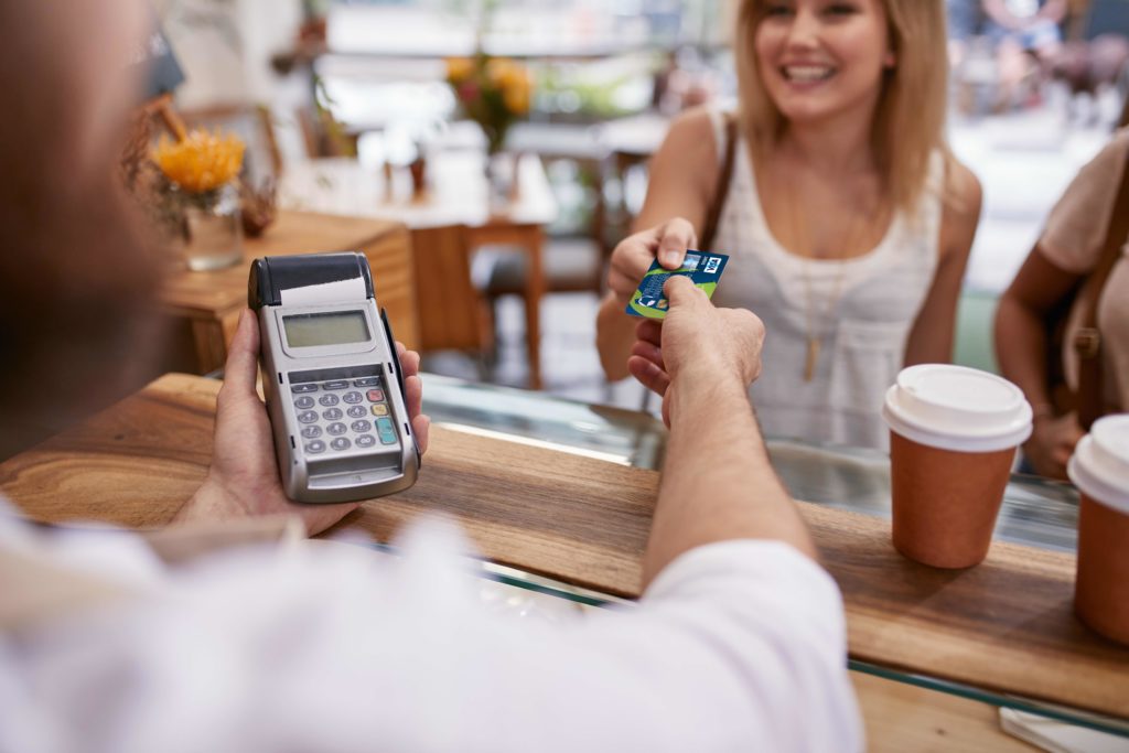 Customer paying for their order with a credit card in a cafe. Bartender holding a credit card reader machine and returning the debit card to female customer after payments.