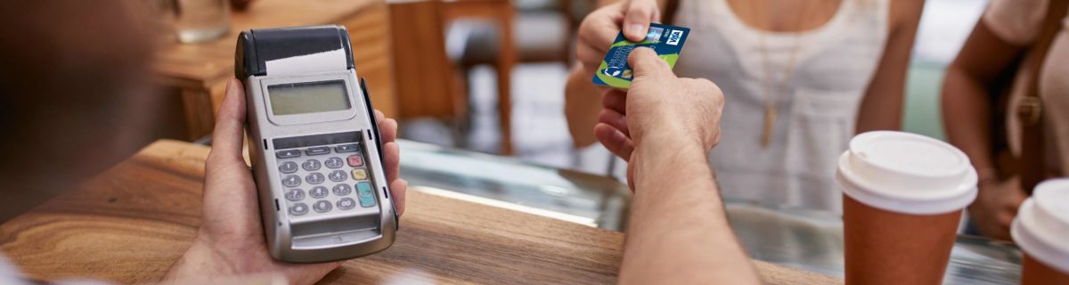 Customer paying for their order with a credit card in a cafe. Bartender holding a credit card reader machine and returning the debit card to female customer after payments.