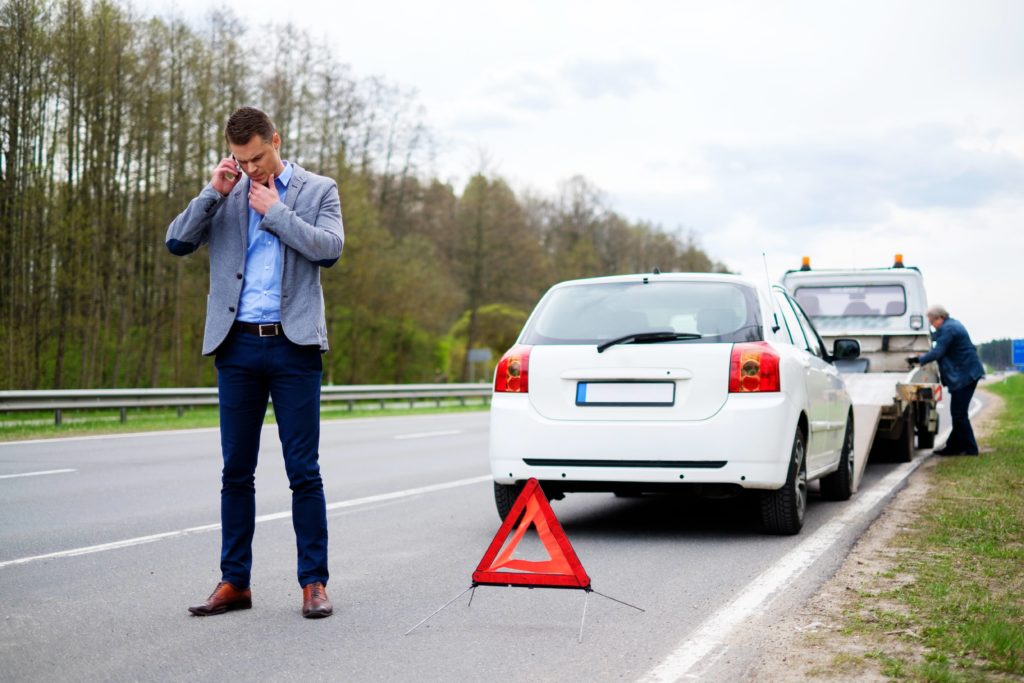 Photo of wrecker loading car with owner on cell phone